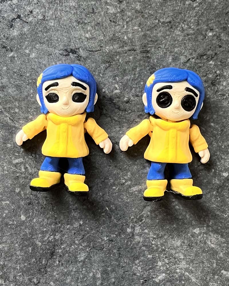 Coraline mini figures with eerie black button eyes, yellow raincoat, and blue hair, inspired by gothic stop-motion style.