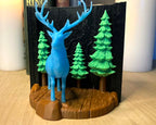 Blue deer figurine with green trees on a wooden base against a black background