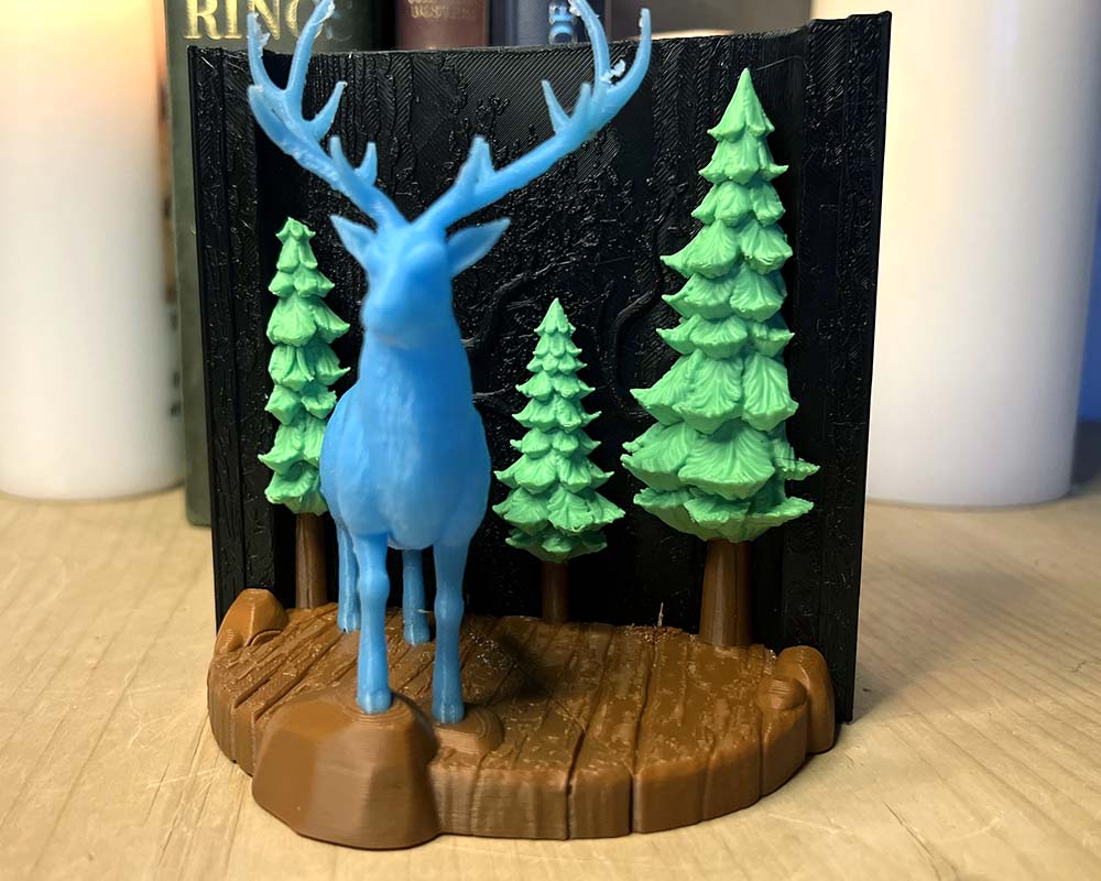 Blue deer figurine with green trees on a wooden base against a black background