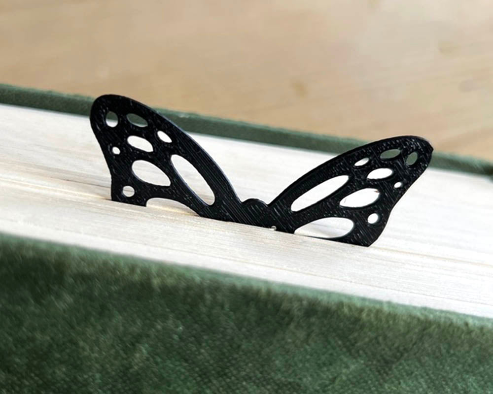 Black butterfly-shaped bookmark on a book with a wooden surface in the background
