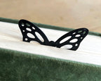 Black butterfly-shaped bookmark on a book with a wooden surface in the background