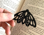 Butterfly-shaped black metal bookmark held over an open book