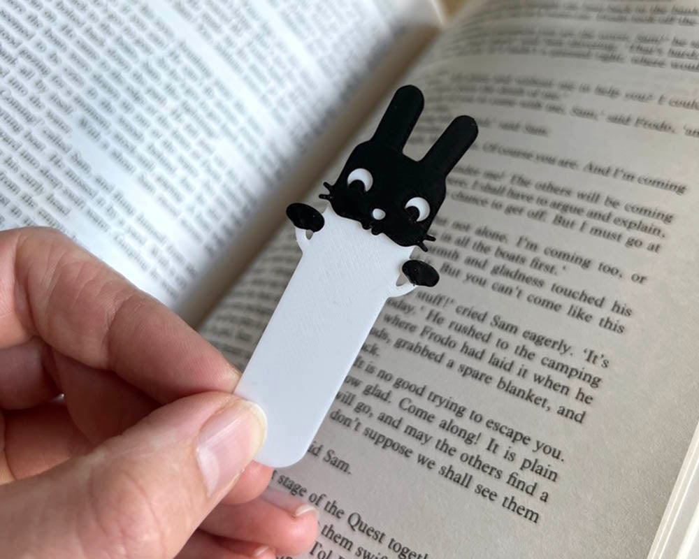 Black bunny-shaped bookmark on a white page held over an open book